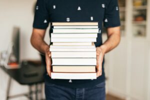 pexels-photo-4218982-4218982 A person holding a stack of books indoors, capturing the essence of knowledge and learning.